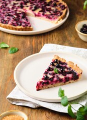 Shortcrust pastry tart with black сurrant and sour cream filling on a ceramic plate on a wooden background. Rustic style. blackcurrant recipes