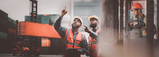 Industrial worker works with co-worker at overseas shipping container yard. Logistics supply chain...