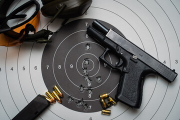 Shooting from a weapon at a target in a shooting range.  A pistol, goggles and earmuffs, and a...