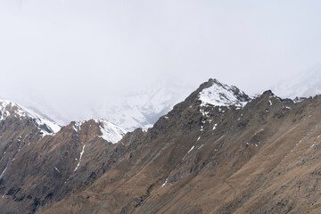 top of the rocky mountain ridge, snow covered mountains in the clouds background, snowy day