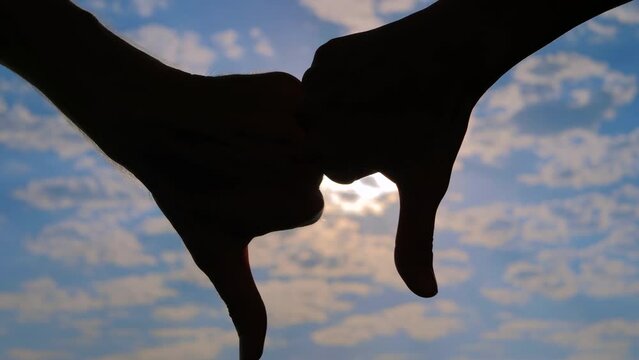 Close up view: silhouettes of persons are showing two thumbs down hand gestures against the cloudy sunset, sunrise blue sky with sun lens flares. Disapproval, negative and decline concept