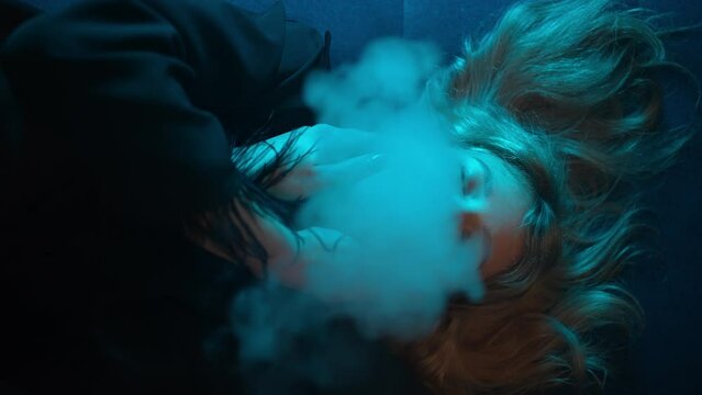 Seductive girl blowing thick smoke in neon light