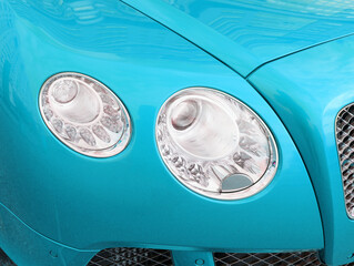 Closeup headlight of modern sport blue car. Car exterior details over city background. Concept of...