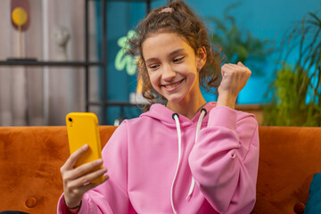 Preteen school girl use mobile smartphone celebrate success win triumph victory, positive test,...
