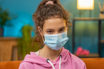 Sick preteen school girl in medical protective face mask looking to camera. Young ill child kid at...