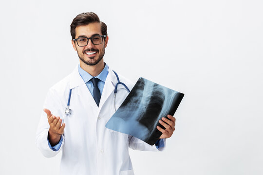 Man doctor in white coat and eyeglasses and stethoscope with a smile looks at patient X-ray images for diagnosis on white isolated background, copy space, space for text, health