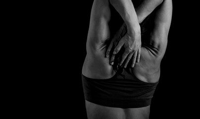 Sporty muscular woman with ponytail doing stretching workout of the shoulders, blades in sport bra, holding hands behind the head on dark grey background with empty space. Black and white