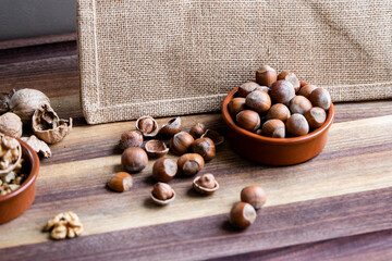 Hazelnuts in a shell and nutshells in ceramic bowl on burlap background
