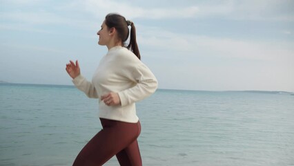Slow motion of young woman staying fit and healthy by jogging on the sandy sea beach at sunset. Importance of an active lifestyle and regular exercise