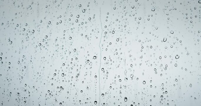 Rain water drops fall down on window transparent glass abstract background. Natural bad weather gray colors.