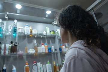 Woman facing a cabinet with lots of beauty items in the bathroom 