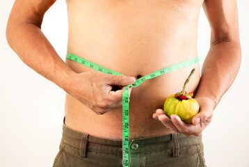 Fat man with belly fat standing holding garcinia and tape measure isolated on white background.