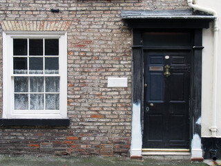 Fototapeta na wymiar front view of a old small english terraced brick house with black painted door and white window