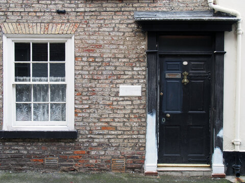 front view of a old small english terraced brick house with black painted door and white window