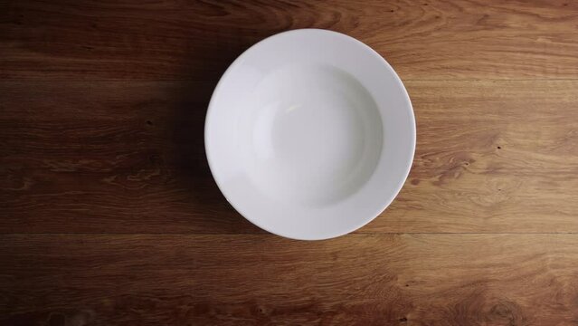 Top view of two male hands placing an empty white plate on a wooden surface.