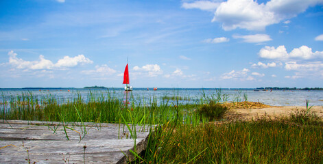 Sailboat with a red sail on a lake with a wooden pier in the foreground
