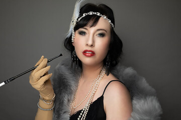 Studio portrait of a caucasian woman wearing 1920s fashion. She is wearing a fringe trimmed dress,...