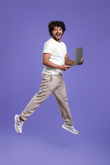 Happy man with laptop jumping on purple background