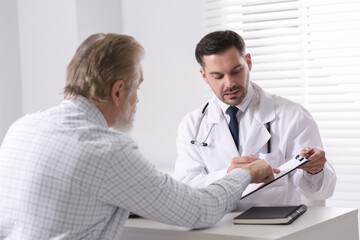 Doctor consulting senior patient at white table in clinic