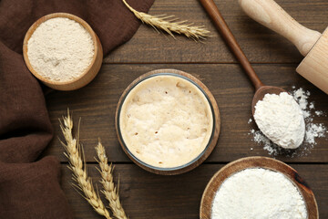 Leaven, flour, rolling pin and ears of wheat on wooden table, flat lay