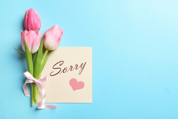 Card with word Sorry and bouquet of tulips on light blue background, flat lay. Space for text