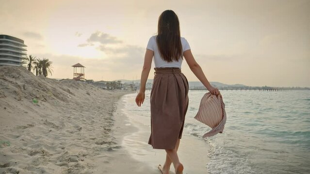 Slow motion of woman enjoying her holiday on the sandy sea beach, walking with a silk scarf. Concepts of travel, journey, and tourism