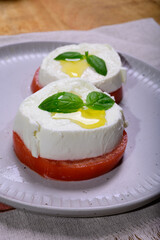 Sliced white ball of Italian soft cheese Mozzarella di Bufala Campana served with fresh green basil and red tomato