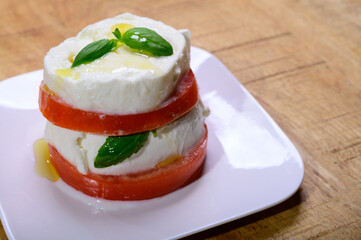 Sliced white ball of Italian soft cheese Mozzarella di Bufala Campana served with fresh green basil and red tomato