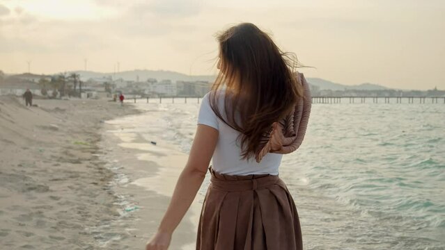 Portrait of happy laughing playful woman runs and spins on the andy sea beach at sunset while looking in camera