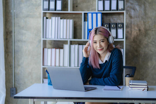 Asian Female College Student Wearing Headphones Studying Online With Laptop Computer Surfing Internet Meeting Studying Online, Smiling Happily At Home.