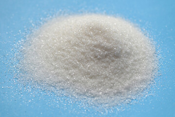 Obraz na płótnie Canvas heap of sugar on blue background, white sugar for food and sweets dessert candy heap of sweet sugar crystalline granulated