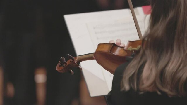 A slow motion video of a musician playing the violin in a classical symphony orchestra