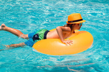 Fototapeta na wymiar Kid boy relaxing in pool. Child swimming in water pool. Summer kids activity, watersports. Fashion summer tanned kid in hat and suglasses. Summer travelling.