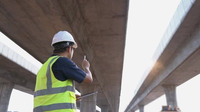 Asian engineer handsome man  using tablet to record electronic data on construction site of concrete highway bridge.