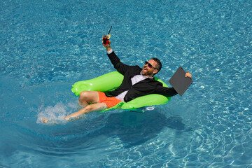 Businessman in suit with laptop in swimming pool. Crazy business man on summer vacation. Excited businessman in wet suit in swim pool. Funny business man, crazy comic business concept. Remote working.