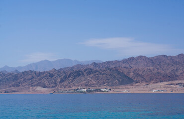 Fototapeta premium Yachts and boats moored in a sea harbor of Sharm El-Sheikh, view on a coast with panorama of mountains and lighthouse. Mountain landscape with tourist cruise boats near the Ras-Mohammed Reserve.