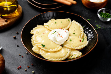 Boiled dumplings with potatoes served with sour cream. Traditional Ukrainian or Russian food. Black background. 