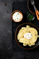 Boiled dumplings with potatoes served with sour cream. Traditional Ukrainian or Russian food. Black background. top view