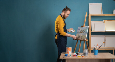 Young man painting on easel with brush in artist studio. Male artist working on painting in studio