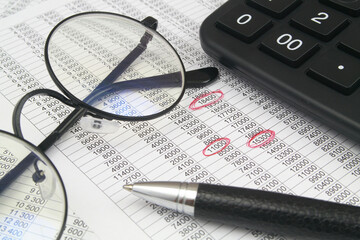 Financial data verification concept. Calculator, pen and eyeglasses on documents with data close up.