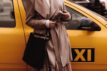 Female figure in the brown long overcoat against the yellow taxi. Outdoor portrait in daylight....