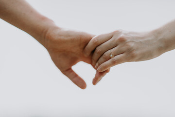 A couple holding hands with a gold engagement ring against a light sky