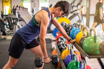 Sportswoman Taking Dumbbell From Rack While Standing In Gym