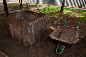 Still life with a wooden compost bin and wheelbarrow. Close up DIY compost bin to improve the...