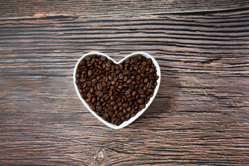 Coffee heart made of coffee beans on wooden background. Coffee in a heart-shaped bowl. Brown heart. Love coffee concept. Copy space. Top view.