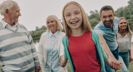 Obraz premium Happy multi-generation family holding hands while spending time outdoors together