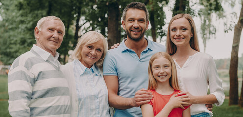 Happy multi-generation family looking at camera while standing outdoors together