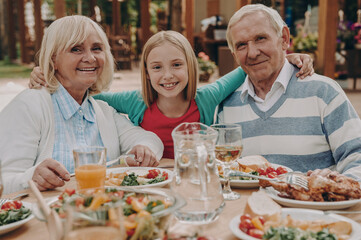 Happy little girl embracing her grandparents while enjoying dinner outdoors together