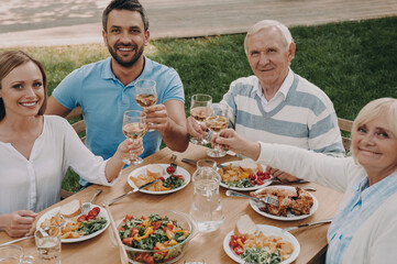 Happy multi-generation family toasting with wine while enjoying dinner outdoors together