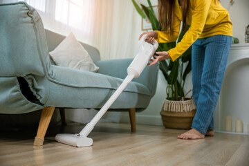 Housewife female dust cleaning floor under sofa or couch furniture with vacuum cleaner, Happy Asian...